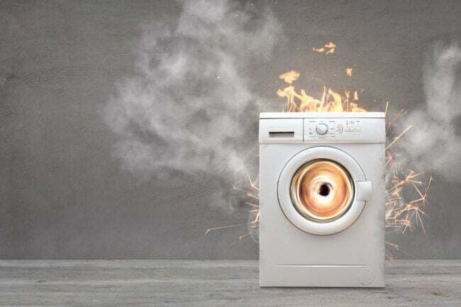 máquina de lavar branca em sala vazia cinza superaquecendo com faíscas e chamas