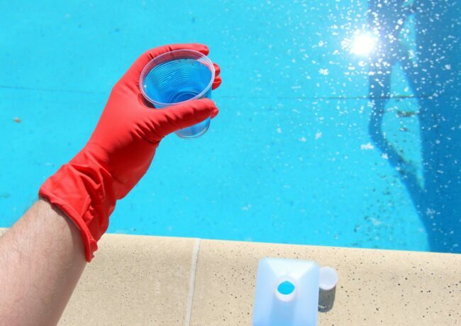 Ręka w czerwonych rękawiczkach trzymająca filiżankę roztworu nad basenem