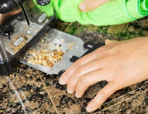 Фотография женской руки, чистящей нижнюю часть кухонного тостера с зеленой тряпкой из микрофибры с каменной столешницей на заднем плане