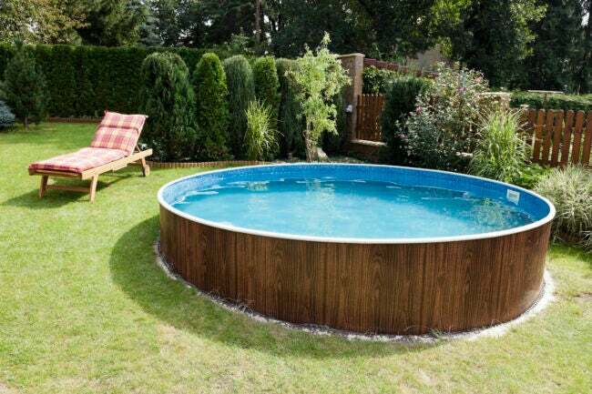 حمام سباحة فوق سطح الأرض محاط بإطار خشبي على حديقة مائلة يضم العديد من نباتات الخصوصية