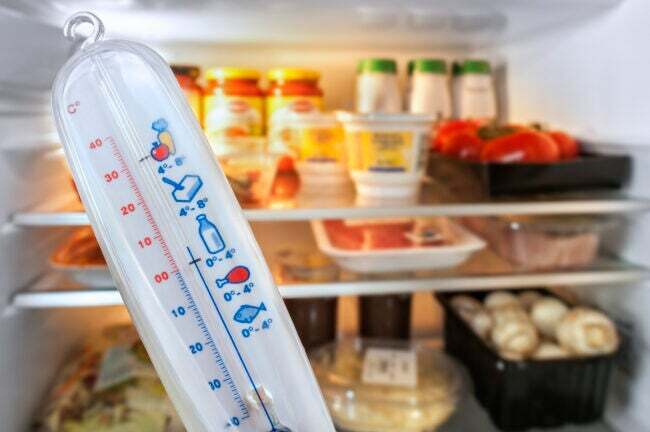 Termometer foran åpent kjøleskap fylt med mat på kjøkkenet