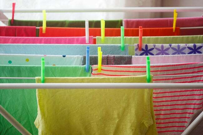 kirkkaanväriset t-paidat roikkuvat riveissä pyykkinarulla värikkäillä pyykkineuloilla