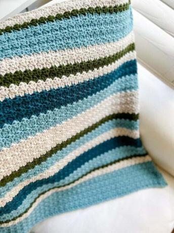 Uma manta de crochê com listras azuis, verdes e creme sobre um assento