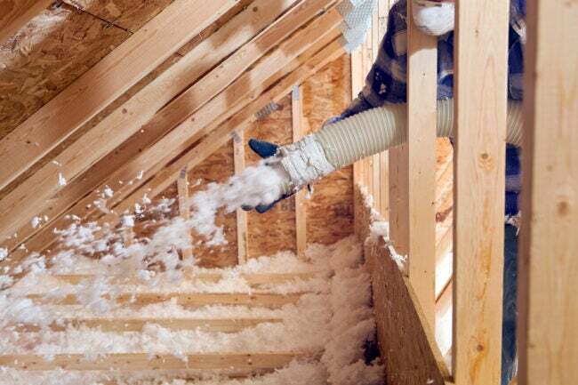 エネルギー効率を高めるために吹き付け断熱材を屋根裏の床に吹き付ける作業員