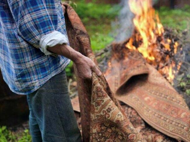 Човек хвърля килим в огън