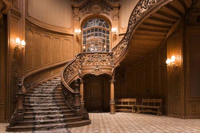 Una escalera de carpintería elaboradamente tallada serpentea en un vestíbulo de entrada con paneles de madera.