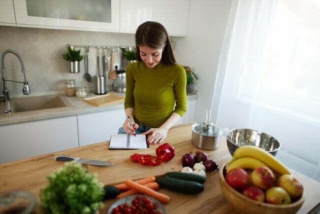 Mlada ženska bere kuharsko knjigo v kuhinji in išče recept