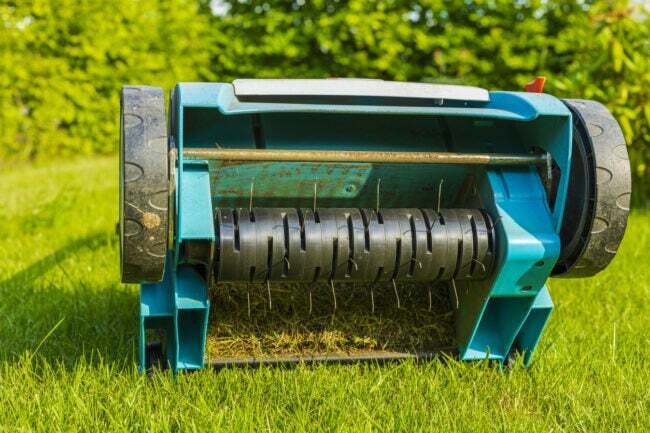 分離された緑の芝生に電動芝生エアレーターのクローズ アップ表示。 園芸機械のコンセプト。