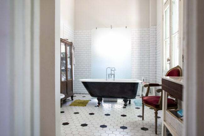 Egy-fekete szabadon álló fürdőkád egy-egy-fekete-fehér vintage-fürdőszobában ül, antik bútorokkal.