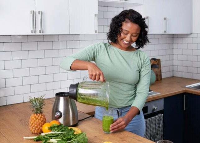iStock-1419300138 tehosekoittimen puhdistaminen Nuori monikansallinen nainen kaataa raikkaan vihreän smoothien keittiössä olevasta tehosekoittimesta stock photo.jpg
