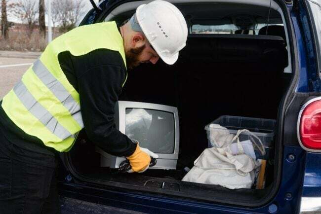 Een sanitairmedewerker die een oude tv uit een kofferbak haalt voor recycling van elektronisch afval.