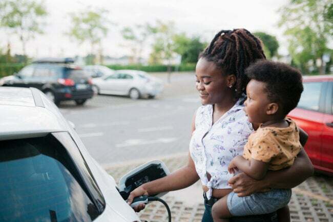 iStock-1412460130 problémák az elektromos autókkal Anya tartja a fiát, miközben tölti elektromos járművét