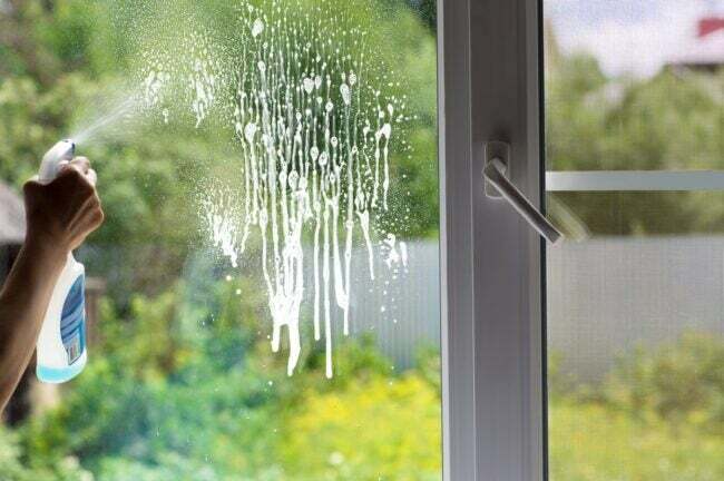 खिड़की पर सफाई का घोल छिड़कता व्यक्ति