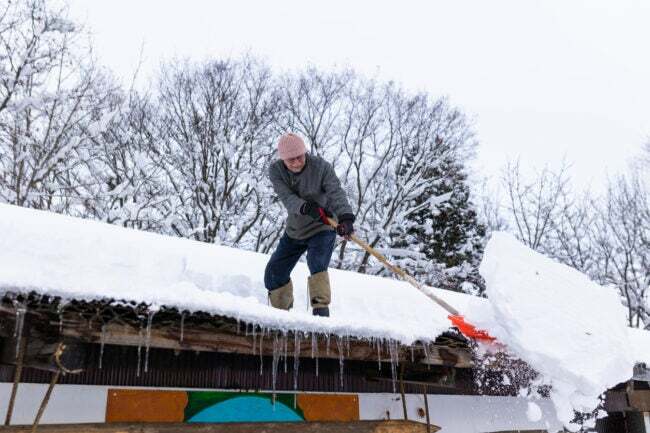 Un uomo spala la neve sopra un tetto innevato.