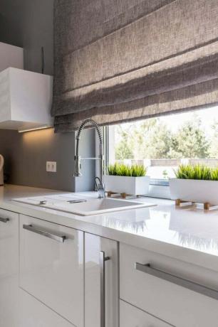 Eine kleine Küche mit großem Fenster, das von einem grauen Raffrollo bedeckt ist.