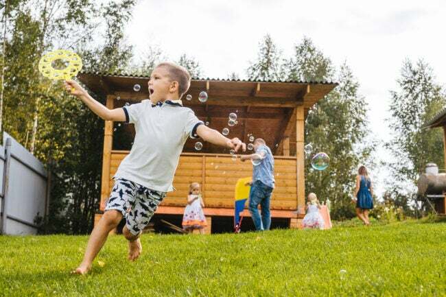 小さな男の子はシャボン玉を吹きながら走ります。 裏庭、背景に家族。