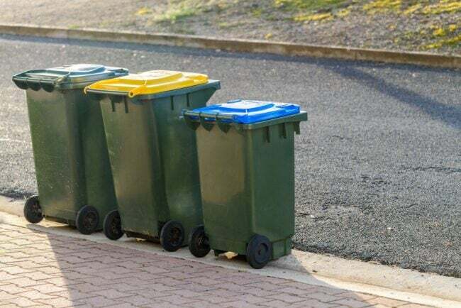 Tre contenitori per rifiuti e riciclaggio sul marciapiede davanti a una casa.
