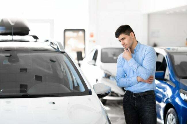 Homme pensant examiner un crossover blanc chez un concessionnaire automobile