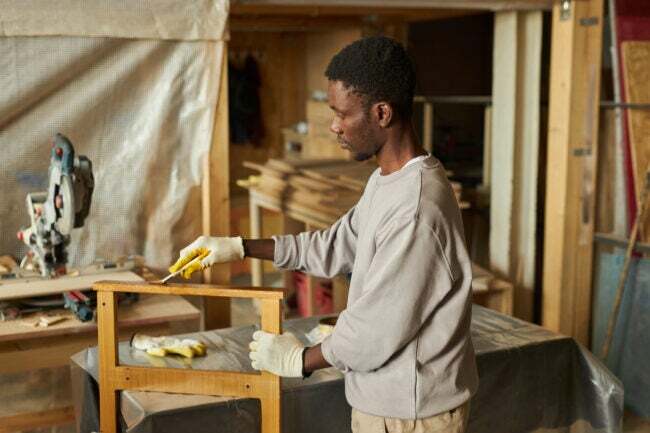 Bočný pohľad na portrét mladého afroamerického muža, ktorý opravuje drevený nábytok v dielni