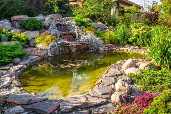 arka bahçede taşlar ve şelale bulunan büyük su özellikli gölet