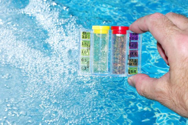 Uma mão segurando um kit de teste de água com fundo de água da piscina.