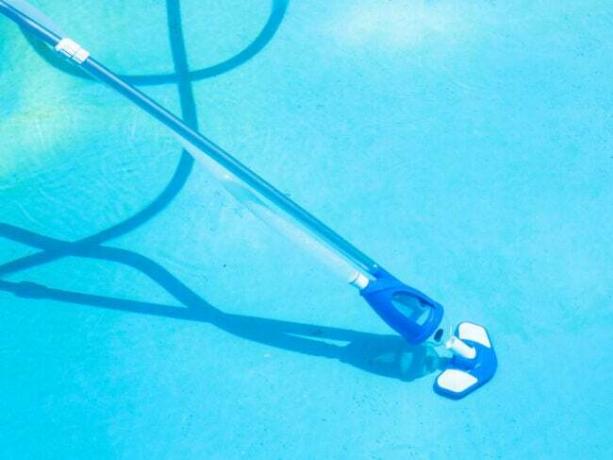 Den bedste håndholdte støvsuger på en forlængerstang med en slange påsat og i brug til at rense bunden af ​​en pool.