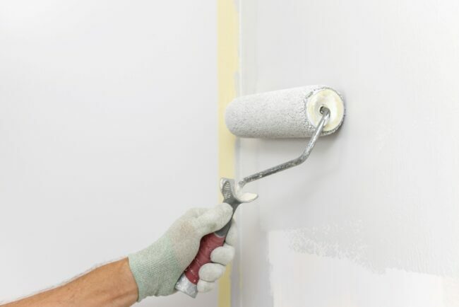 Рука у рукавици користи ваљак за фарбање зидова