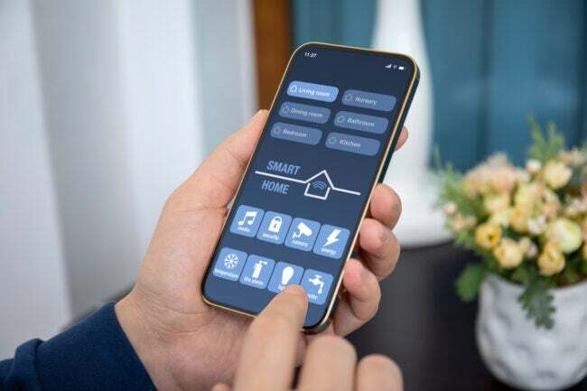 férfi kezében tartja telefon intelligens otthon alkalmazás a képernyőn a szoba házban