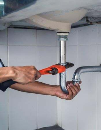 Pár rukou používá nástroj k opravě vodovodního potrubí pod dřezem.