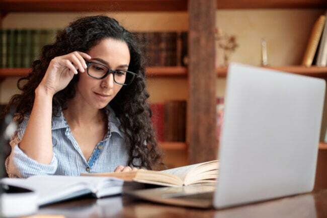Mladá dáma čtení knihy sedí u stolu dotýká brýle