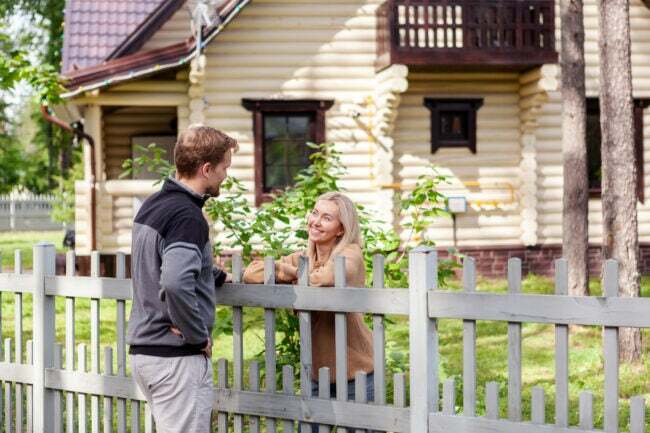 Muž sa stretáva s usmievavou susedkou na vidieku a rozpráva sa s ňou cez plot.