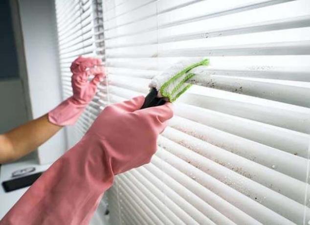 orang dengan sarung tangan karet merah muda membersihkan tirai jendela dengan sikat