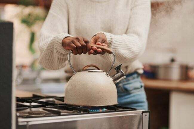 жінка ставить чайник над запаленою конфоркою газової плити