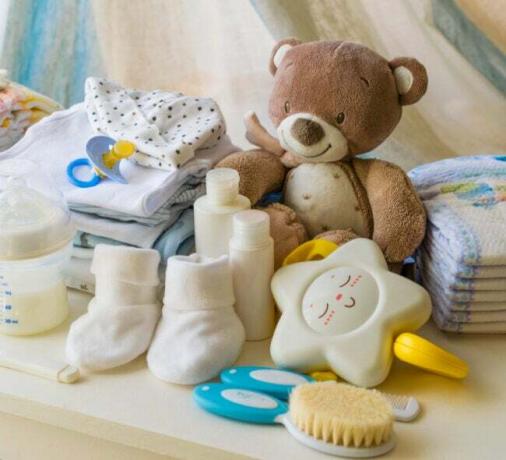 Brauner Teddybär, Schnuller, sternförmiges Spielzeug, Babyschuhe und Babyflasche auf einer weißen Kommode