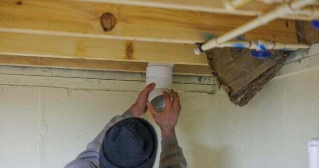 Instalacja systemu ograniczającego radon. Pracownik instaluje rurę w suficie piwnicy.