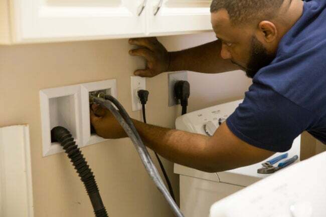 човек проверава црева машине за прање веша иза машине за прање веша