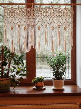 Beige macramé hangend in een raam met planten eronder