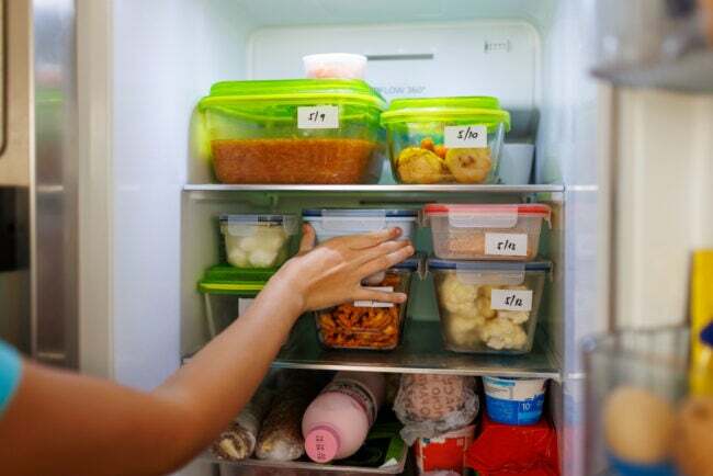 Zbytky jídla zabalené v krabicích uvnitř domácí lednice s napsanými daty.