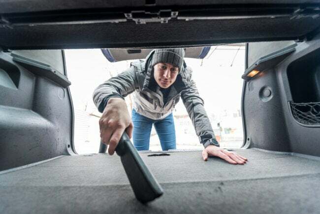 tarefas de manutenção do carro - homem usando vácuo no porta-malas do carro
