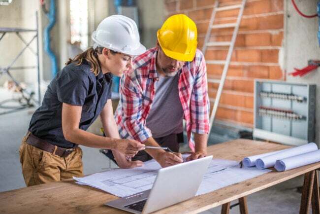 Женщина-архитектор и женщина-строитель прораб смотрят на план, используя ноутбук на строительной площадке.