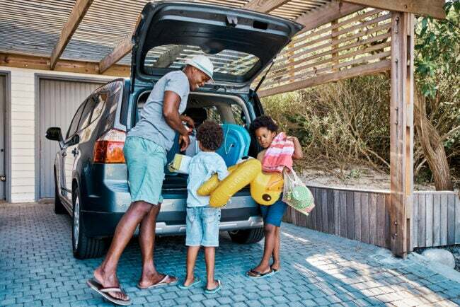 幸せな父親と若い息子が休暇に行く準備をしているオープンバンのトランクに荷物を積み込む