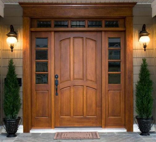 gyönyörű sötét fából készült bejárati ajtó, amelyet két ház lámpa szegélyez a verandán