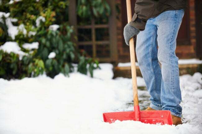 Кокосовое масло использует мужчина, сгребающий снег на тротуаре возле дома