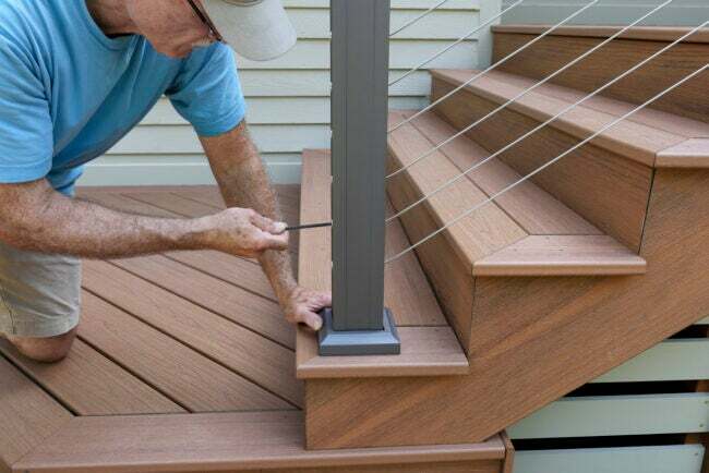 Pekerja menggunakan kunci pas allen untuk mengencangkan pagar kawat pada dek kayu komposit baru dengan tangga.