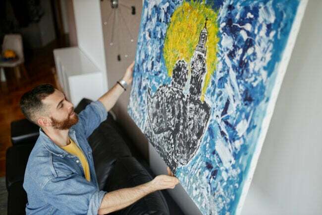 Homem com barba pendurando uma pintura na parede de sua sala de estar