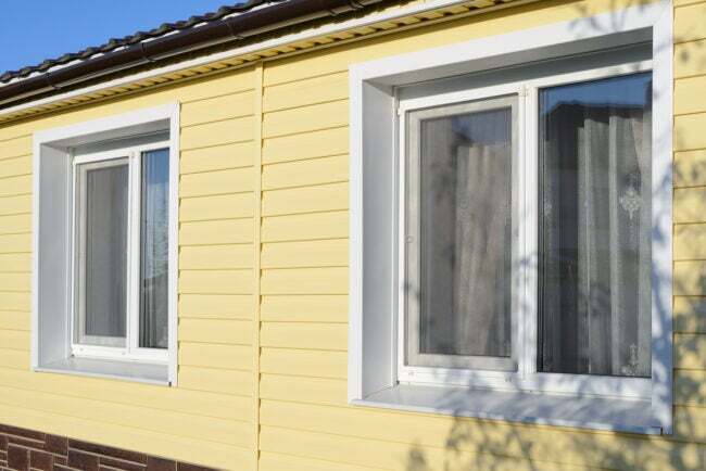 青い空を背景に黄色のビニールのサイディングと 2 つの窓がある家の側面の斜めの眺め