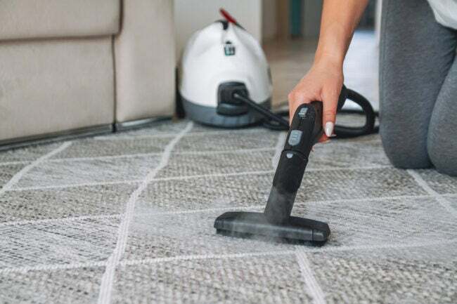 Žena čisti tepih parnim čistačem