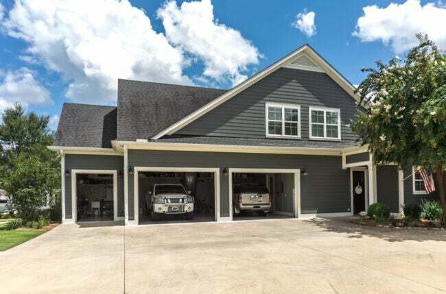 私道とオープンガレージに駐車された2台の車のある大きな灰色の家 