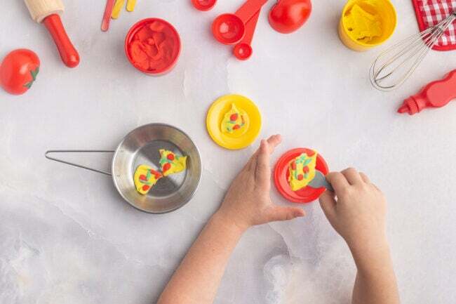 플레이 반죽과 장난감 베이킹 물건으로 음식을 만드는 소년의 손을 머리 위로 봅니다. 