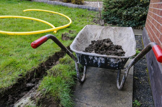 Carretilla llena de tierra después de cavar una zanja en el fondo de un césped para instalar un canal de drenaje.
